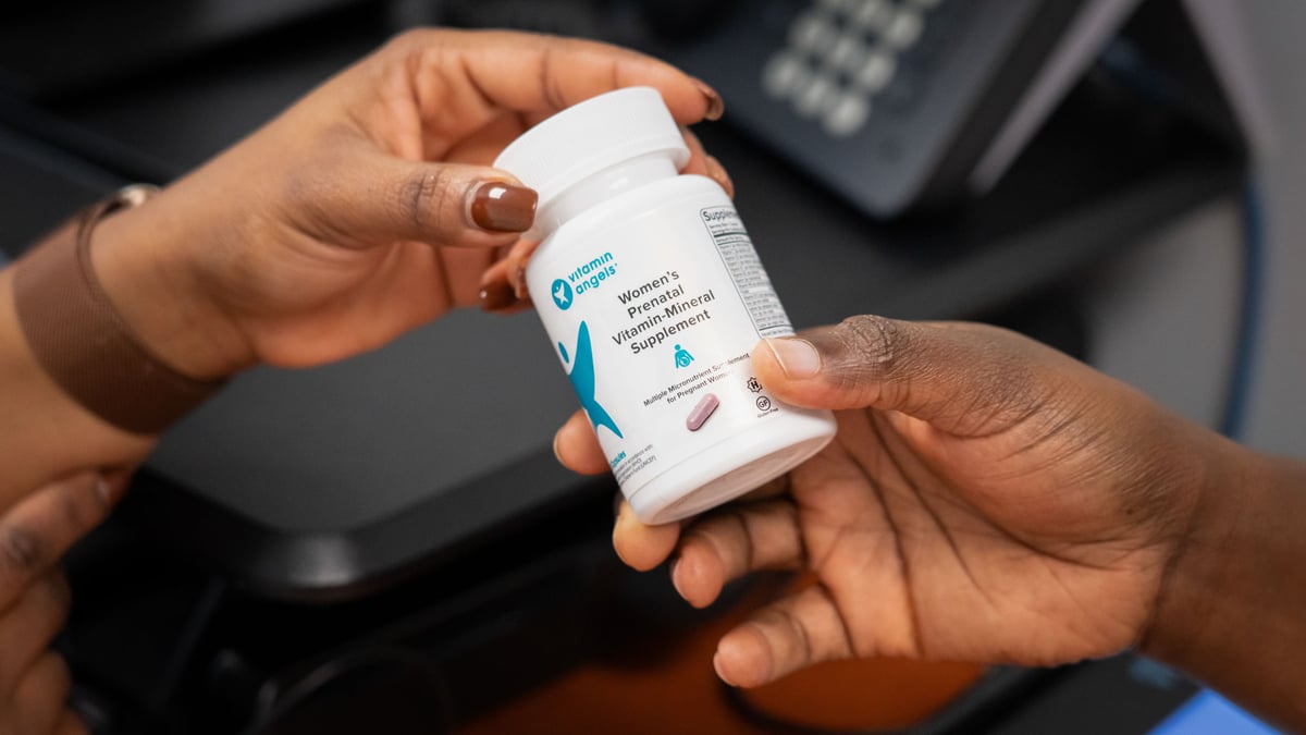 A bottle of prenatal vitamins and minerals passed between two hands